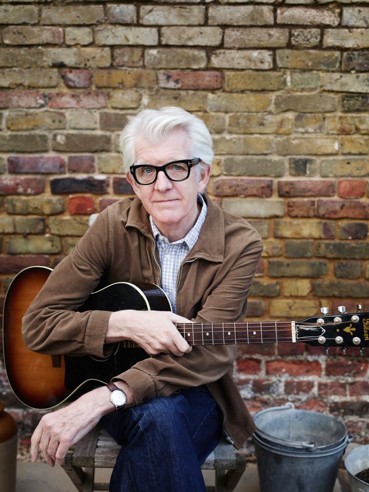 Nick Lowe poses with an acoustic guitar.